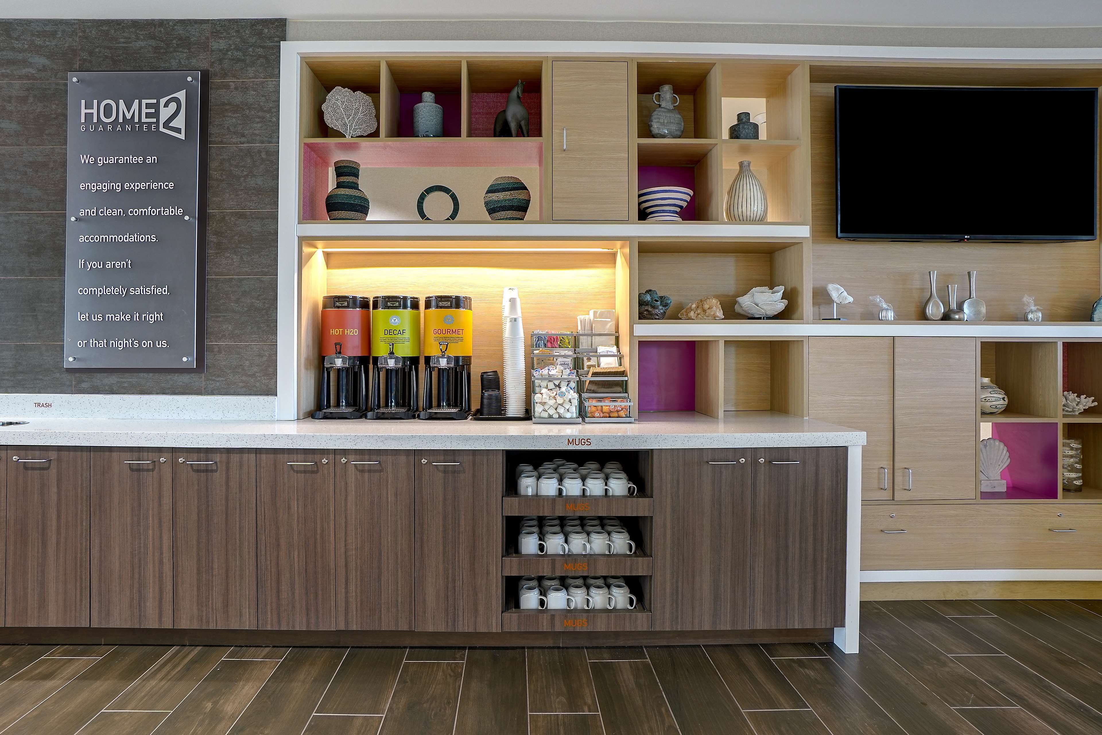 A modern kitchen with a built-in coffee station, a flat-screen TV, and a sign about home guarantee.