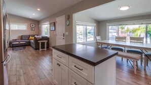 A modern kitchen with a central island, a dining area with a long table, and a living area with a sofa and a coffee table. - NEW Super Clean 3 Bed / 2 Bath Home - Fully Loaded (San Diego)
