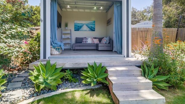 A cozy outdoor seating area with a sofa and cushions, surrounded by a wooden deck and plants. - NEW Super Clean 3 Bed / 2 Bath Home - Fully Loaded (San Diego)