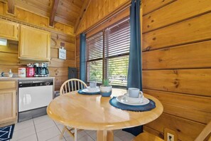 A wooden cabin interior with a dining table set for two, a coffee maker, and a dishwasher. - Location! Smokies Log Cabin, Hot Tub, Fireplace (Pigeon Forge)