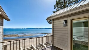 Eine Holzterrasse mit Metallgeländer, die auf einen Strand und ein Gewässer blickt.