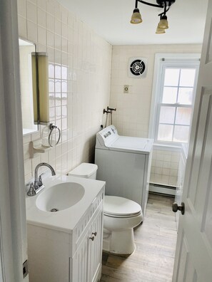A bathroom with a white sink, toilet, and vanity. There is a window with a view of the outside. - Elegant and Bright Ocean Block Home w/ Private Balcony, BBQ & Patio (Seaside Park)