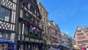 Eine historische europäische Straße mit traditionellen Fachwerkhäusern, Flaggen und einer belebten Menschenmenge.