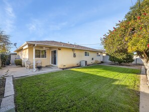 Une maison de plain-pied avec une pelouse bien entretenue, une terrasse avec des chaises et une antenne parabolique.