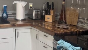 A modern kitchen with white cabinets, a wooden countertop, a stove, and a hanging rack for glasses.