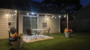 A backyard patio with a table and chairs, string lights, and potted plants.