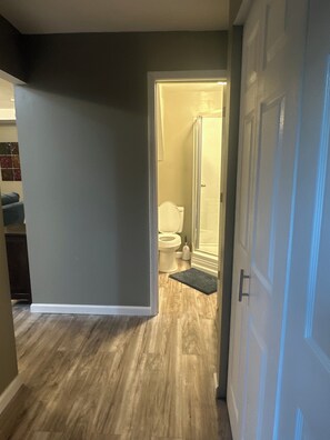 Un pasillo con piso de madera que conduce a un baño con inodoro y ducha.