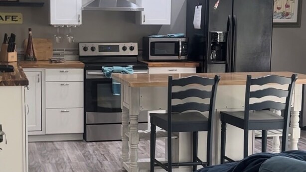 A modern kitchen with white cabinets, a microwave, a stove, and a refrigerator. There is a dining area with a table and chairs.