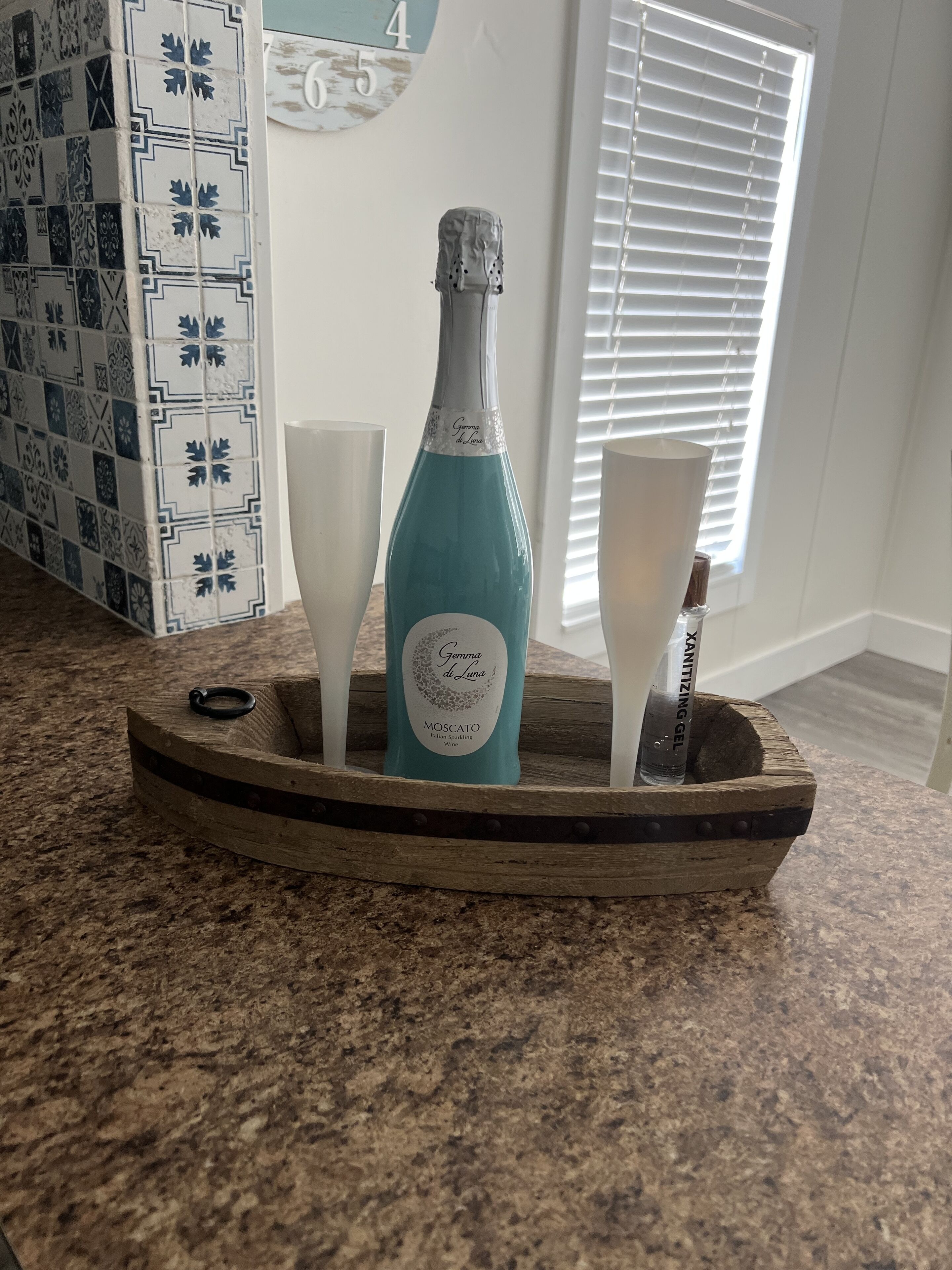 A bottle of sparkling wine on a wooden tray with two glasses, set on a kitchen counter.