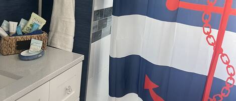Un bagno con tenda da doccia a tema nautico, una decorazione a stella marina e articoli da toilette sul ripiano.