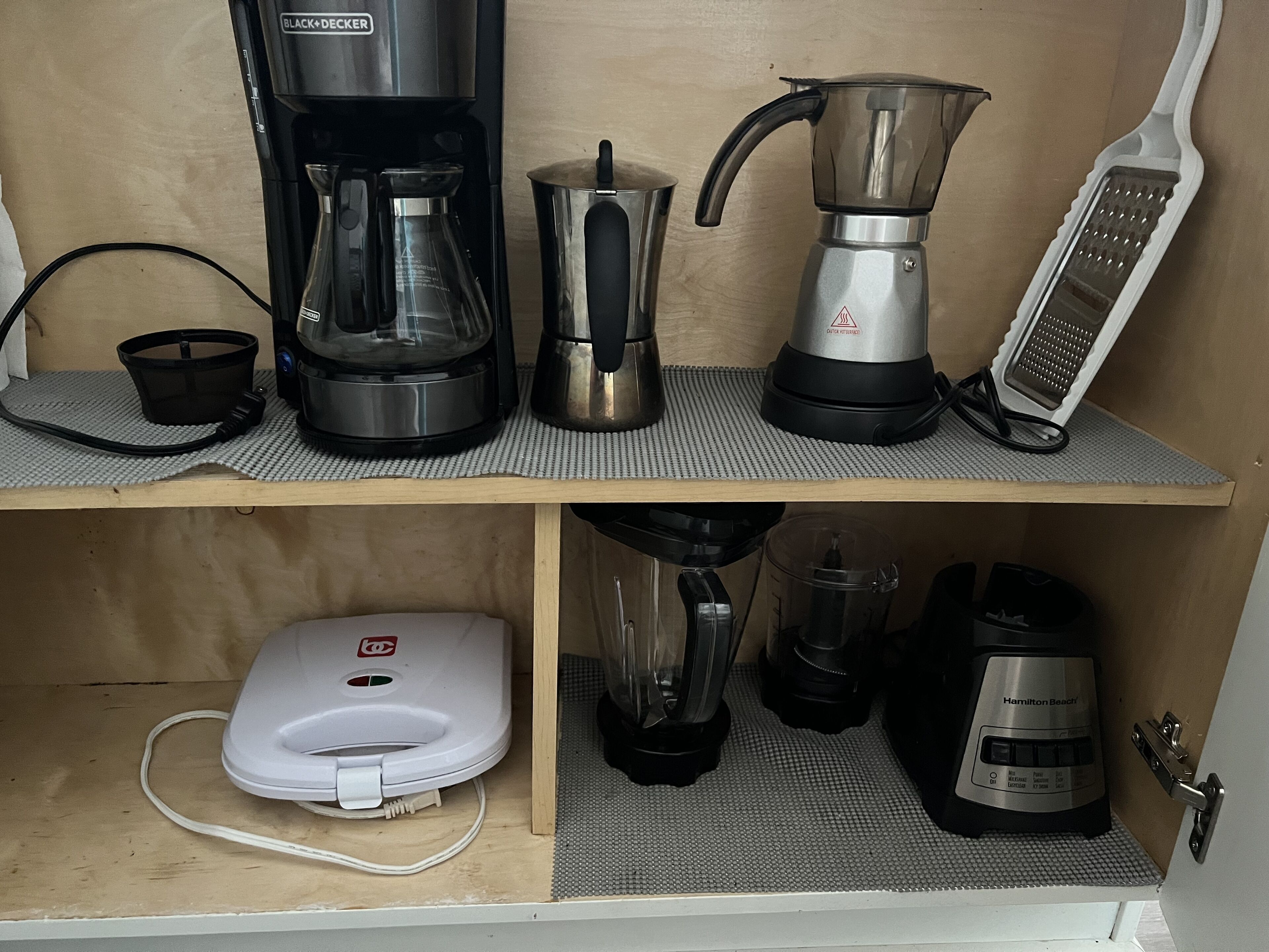 A kitchen with a coffee maker, a kettle, a blender, and a toaster on shelves.