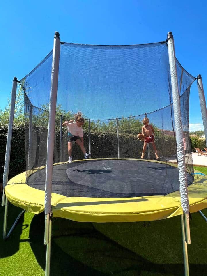A trampoline with a safety net enclosure, surrounded by greenery.