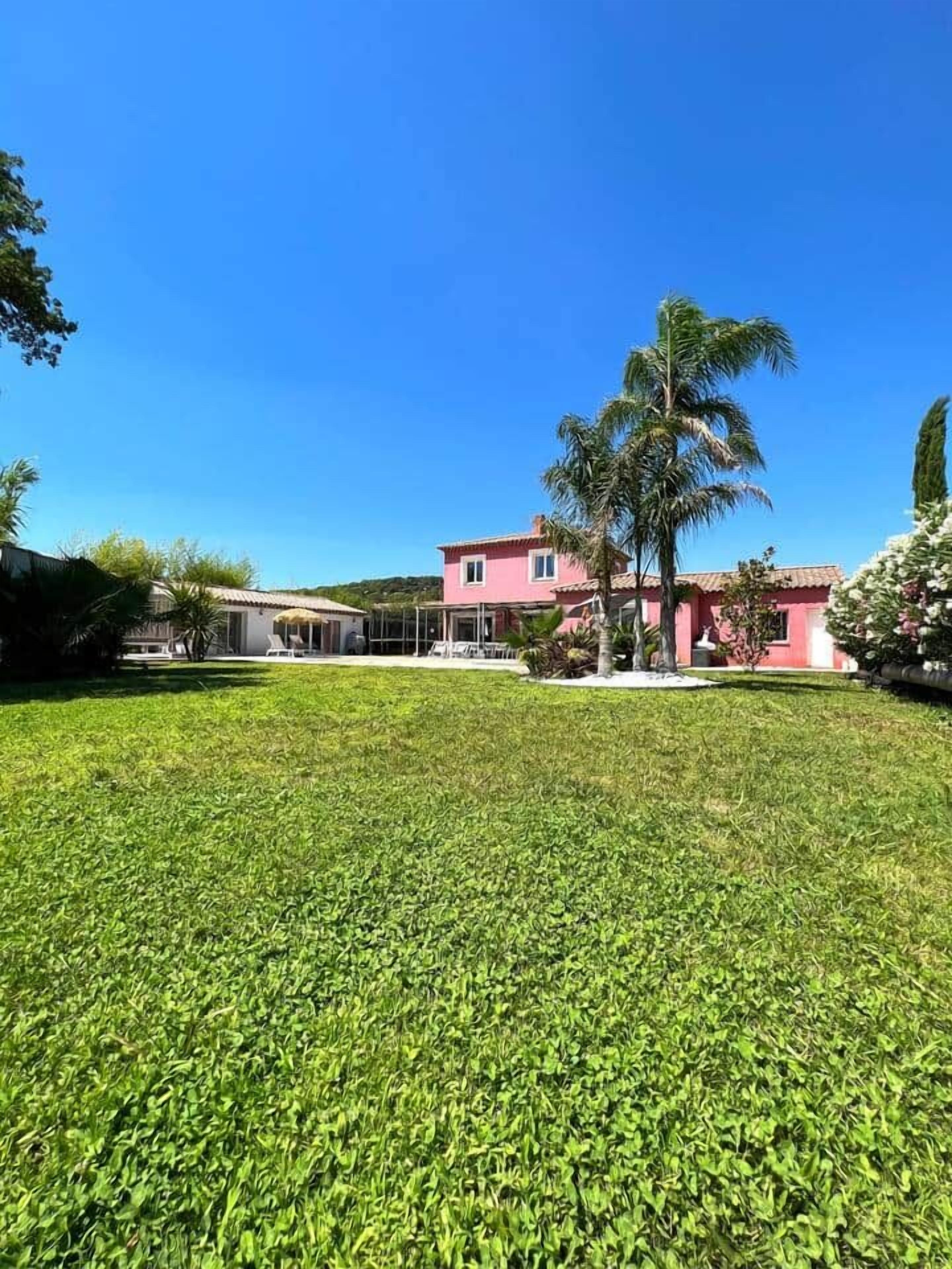 A grassy lawn, a pink building, and a palm tree.