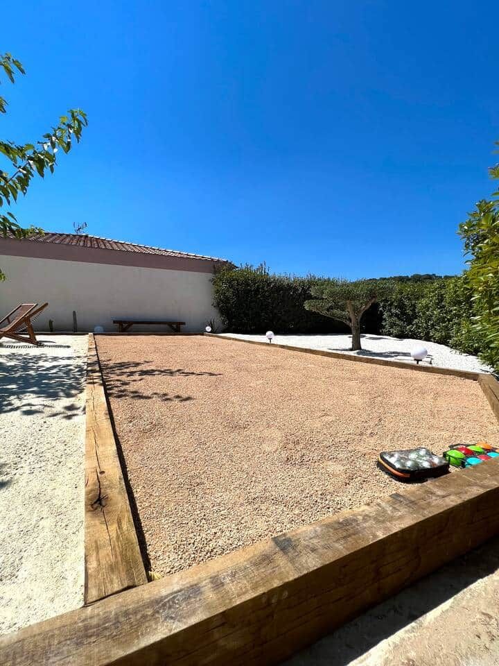 Un espace de patio recouvert de gravier, bordé de bois, avec un banc et un arbre en arrière-plan.