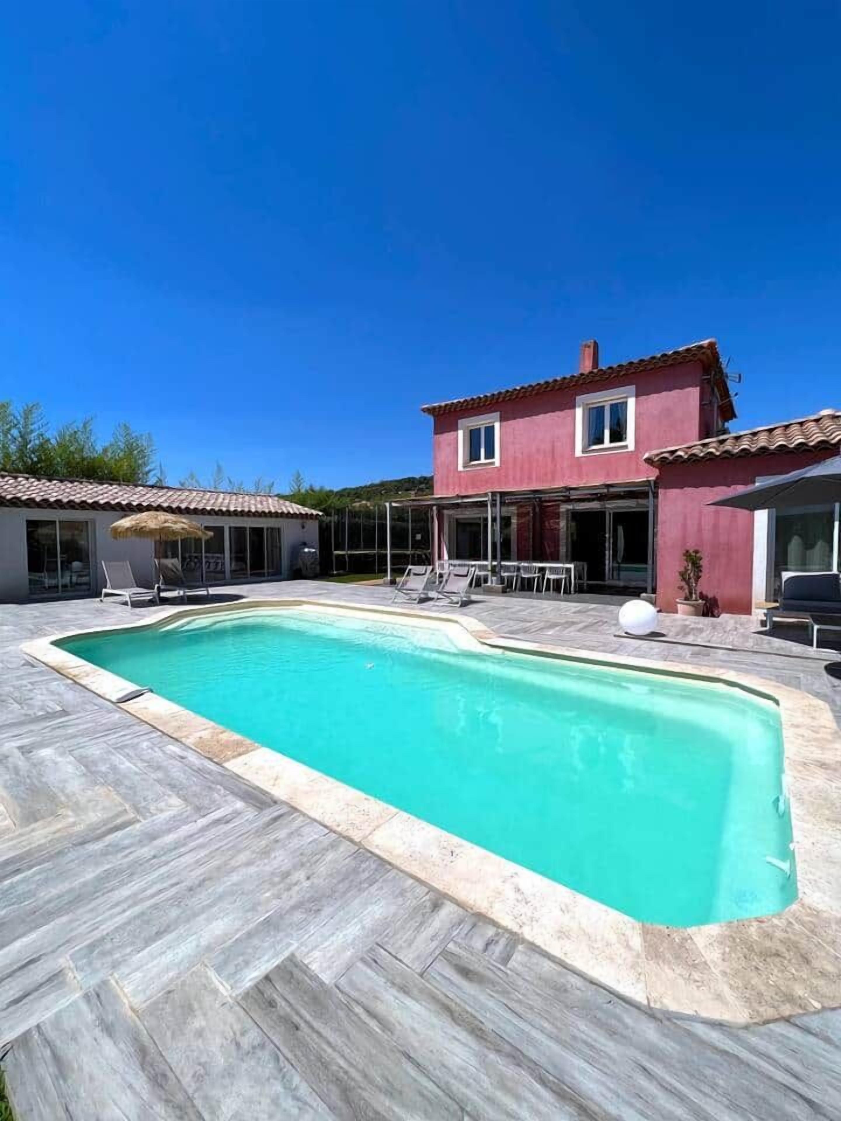 A two-story house with a swimming pool, outdoor furniture, and a clear blue sky.