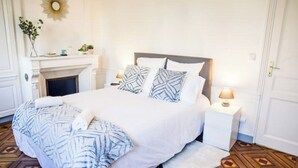 A neatly arranged bedroom with a bed, bedside tables, a fireplace, and a door. - Le Canyon Rouen Centre by MyFrenchPAT Votre Escapade Terrasse! Parking possible
 (Rouen)