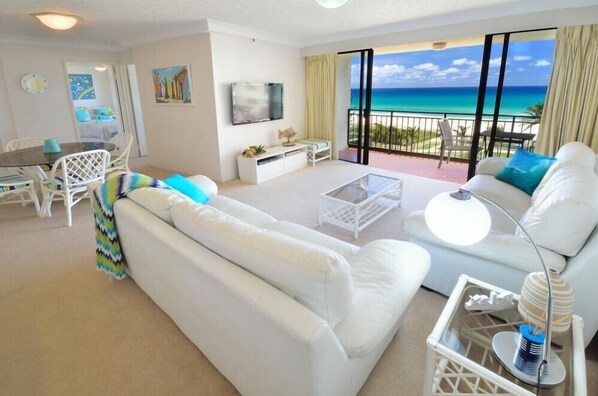 Een moderne hotelkamer met een groot balkon, witte meubels en uitzicht op zee.