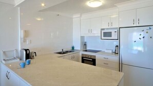 A modern kitchen with white cabinets, a stainless steel refrigerator, a microwave, and a coffee maker. - Ocean View Waterfront Apartment Gold coast (gold coast)