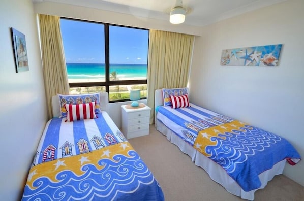 Una habitación con dos camas, una ventana con vista al mar y una pequeña mesa con lámpara.