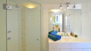 A modern bathroom with a glass-enclosed shower, a white sink with a mirror, and neatly folded towels. - Ocean View Waterfront Apartment Gold coast (gold coast)