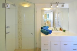 Un baño moderno con ducha de vidrio, un lavabo blanco con espejo y toallas ordenadamente dobladas.