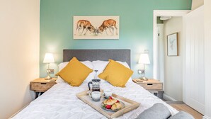 A neatly made bed with a tray of breakfast, two bedside lamps, and a painting of horses on the wall. - 2 bedroom accommodation in Bakewell (Bakewell)