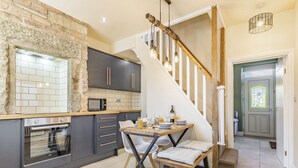 A modern kitchen with a stone wall, dark cabinets, and a wooden staircase. - 2 bedroom accommodation in Bakewell (Bakewell)