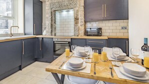 A modern kitchen with dark cabinets, a stone accent wall, a built-in microwave, and a dining area set for breakfast. - 2 bedroom accommodation in Bakewell (Bakewell)