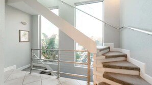 Una escalera con barandilla de metal, paredes blancas y vista a zonas verdes.