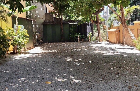 A gravel courtyard with a green gate, trees, and a yellow building.