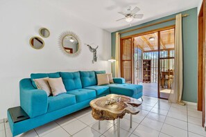 A modern living room with a teal sofa, a wooden coffee table, and a ceiling fan.