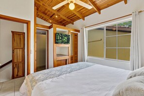 A bedroom with a bed, wooden ceiling, a window with curtains, and a door.