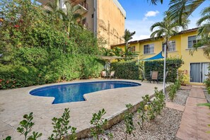 A swimming pool with a curved edge, surrounded by greenery and a paved walkway.