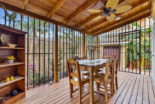 A wooden deck with a table and chairs, surrounded by metal railings and plants.