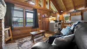 A cozy cabin interior with a wooden interior, a stone fireplace, a dining area, and a living room with a leather sofa.