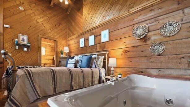 A wooden cabin bedroom with a large bathtub, a bed with striped bedding, and wall-mounted decor.
