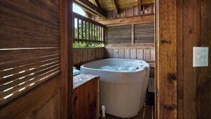 A wooden cabin interior with a hot tub, wooden walls, and a window with blinds.