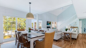 Un salon spacieux avec une grande table à manger, des chaises en osier et un coin salon confortable avec un canapé et des fauteuils.