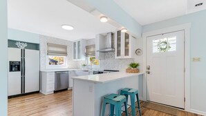 Une cuisine moderne avec des meubles blancs, un îlot central doté de tabourets de bar et un dosseret orné d’un motif en chevrons.