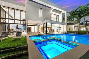 Une maison moderne dotée d’une piscine, de grandes fenêtres et d’un espace salon extérieur.