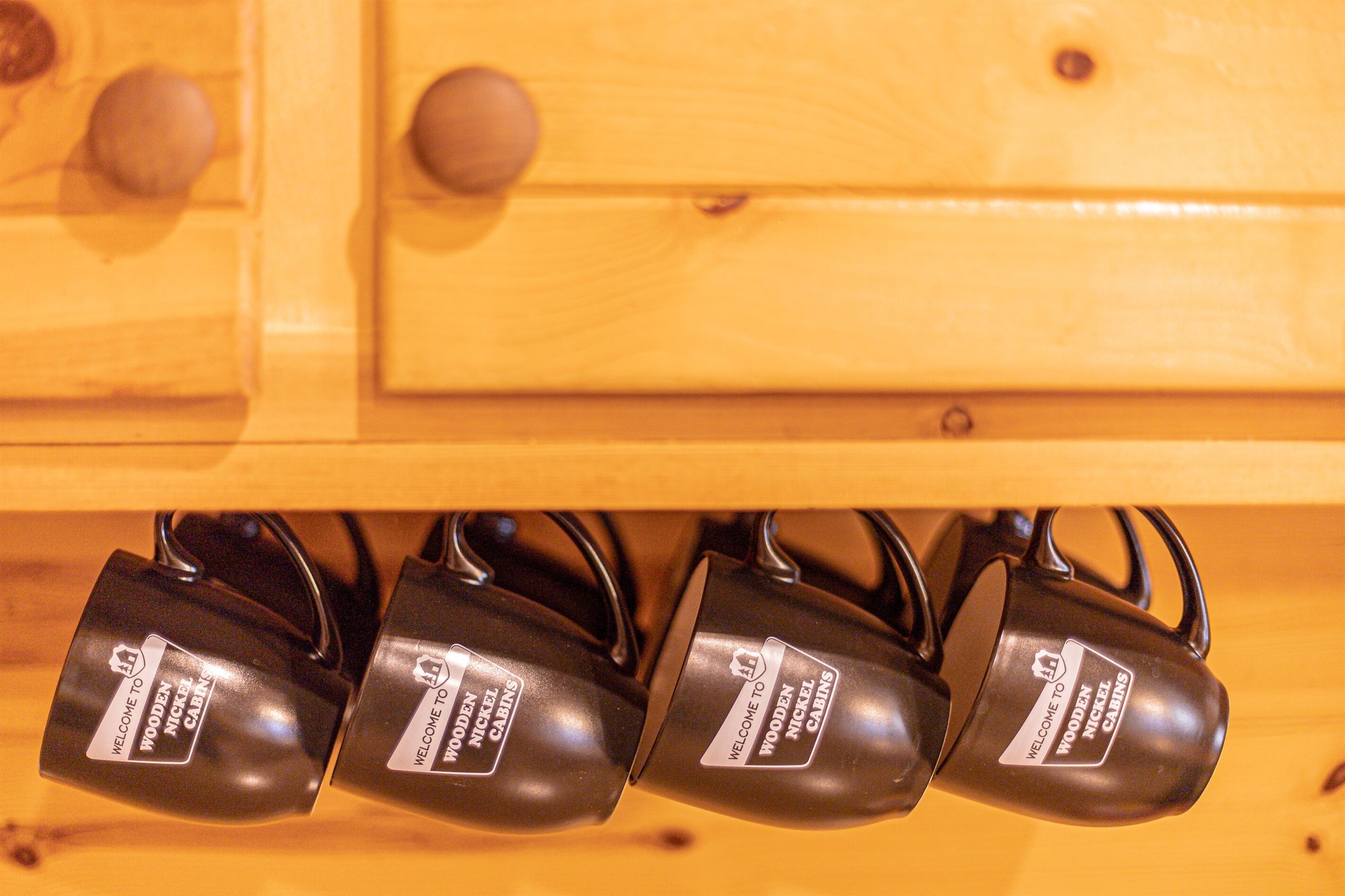 A wooden cabinet with four black metal hooks labeled "Welcome to Wooden Nickel Cabins."