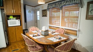 Un coin repas avec une table en bois, quatre chaises et un four à micro-ondes posé sur un meuble.
