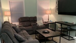 A living room with a sectional sofa, a coffee table, a TV, and a small table with a lamp.