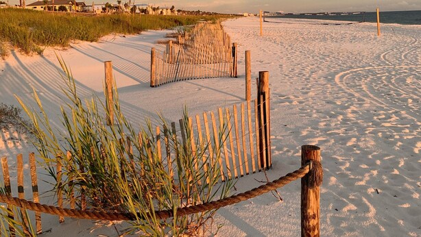 A sandy beach with a wooden fence and a rope barrier.