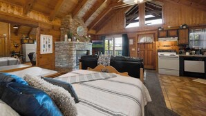A log cabin interior with a large bed, a fireplace, a kitchen, and a dining area. - Location! Cute Studio Log Cabin,Fireplace, Hot Tub (Pigeon Forge)