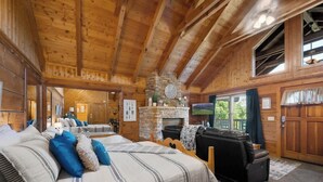 A log cabin interior with a large bed, a fireplace, a sofa, and a television. - Location! Cute Studio Log Cabin,Fireplace, Hot Tub (Pigeon Forge)