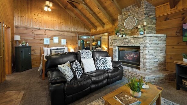 A cozy log cabin interior with a stone fireplace, leather sofa, and a dining area. - Location! Cute Studio Log Cabin,Fireplace, Hot Tub (Pigeon Forge)