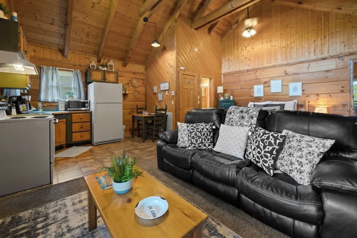 A cozy cabin interior with a dining area, kitchen, and a leather sofa with patterned cushions.