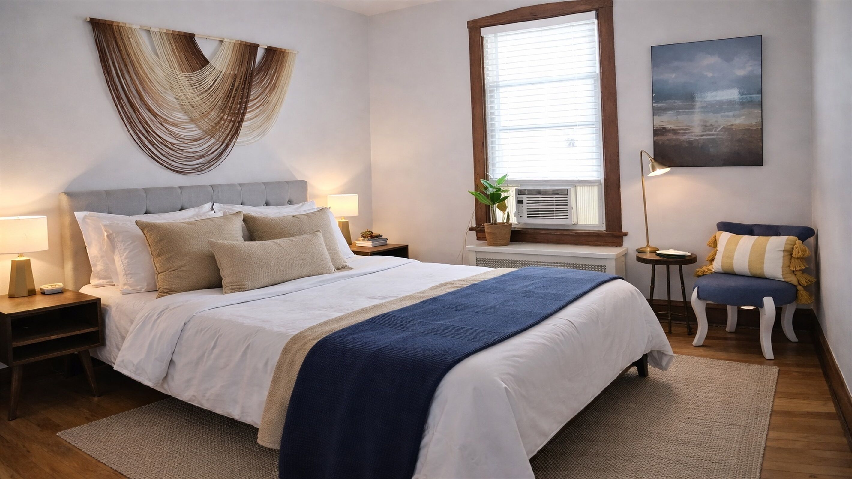 Une chambre bien rangée, avec un lit, des tables de chevet, une fenêtre, une chaise et un climatiseur fixé au mur.