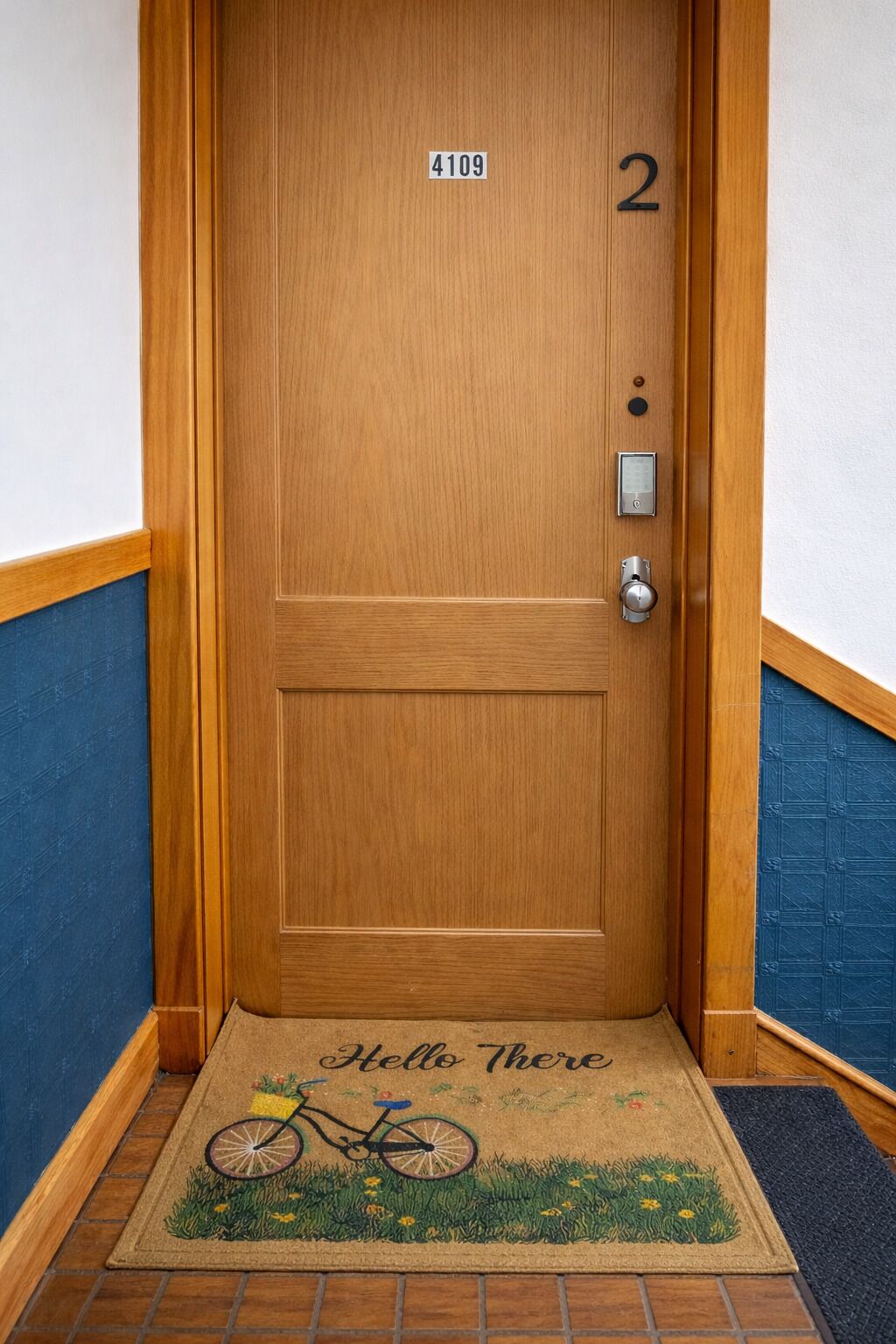 Eine Holztür mit Klingelschild, Tastatur und Fußmatte mit Fahrradmotiv.